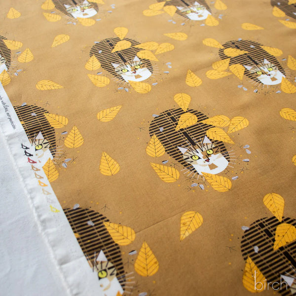 Selvage of Birdwatcher organic cotton poplin fabric by Charley Harper for Birch Fabrics featuring a brown tabby cat among yellow leaves on a golden brown background.
