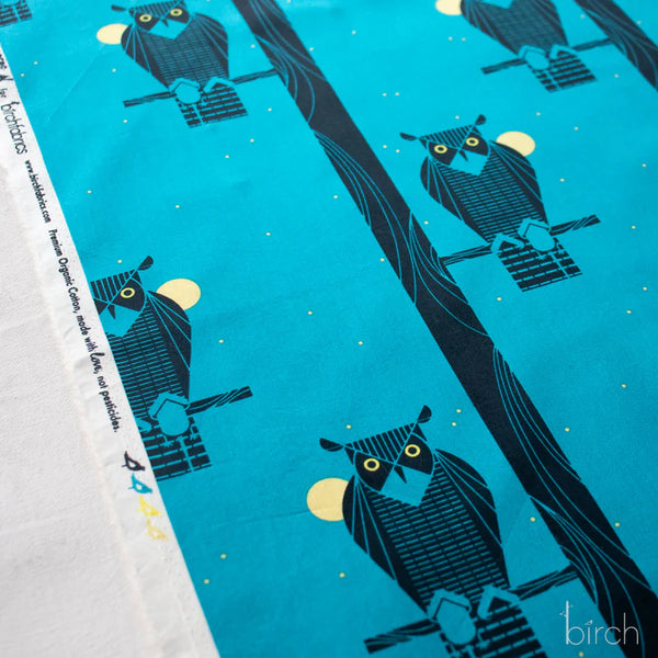 Selvage of Moon Owl organic cotton poplin fabric by Charley Harper for Birch Fabrics featuring a black owl perched on a branch against a rich blue background.
