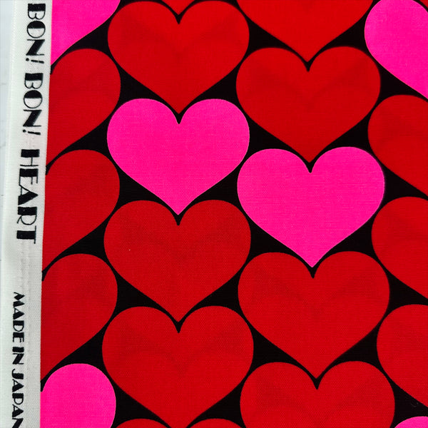 Selvage of Bon Bon Heart cotton Oxford fabric in neon pink and black featuring a large-scale heart print, imported from Japan