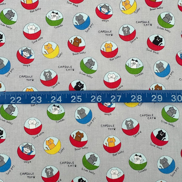 Scale of Capsule Toy Cats cotton canvas fabric in gray by Cotton Kobayashi featuring playful cats inside capsule toy machines on a gray background
