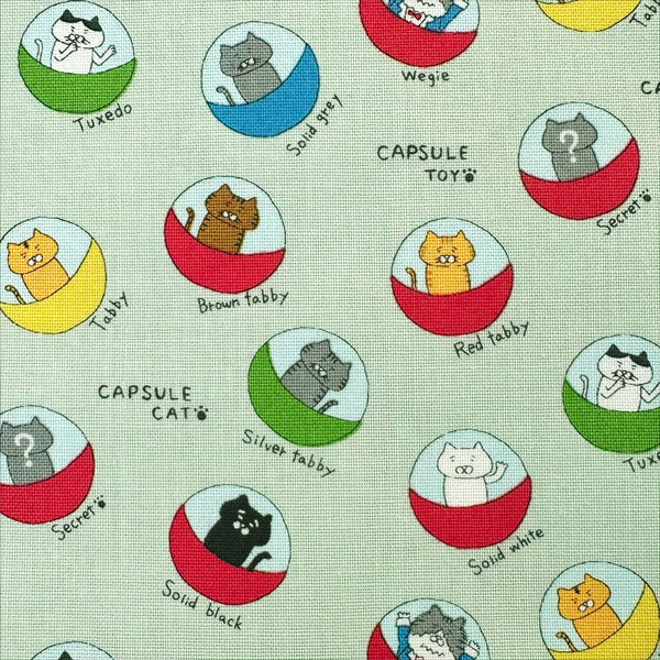 Close up of Capsule Toy Cats cotton canvas fabric in green by Cotton Kobayashi featuring playful cats inside capsule toy machines on a green background
