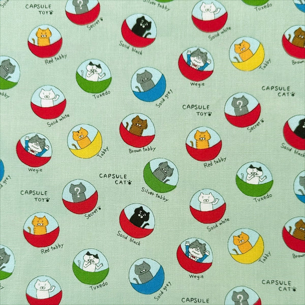 Capsule Toy Cats cotton canvas fabric in green by Cotton Kobayashi featuring playful cats inside capsule toy machines on a green background