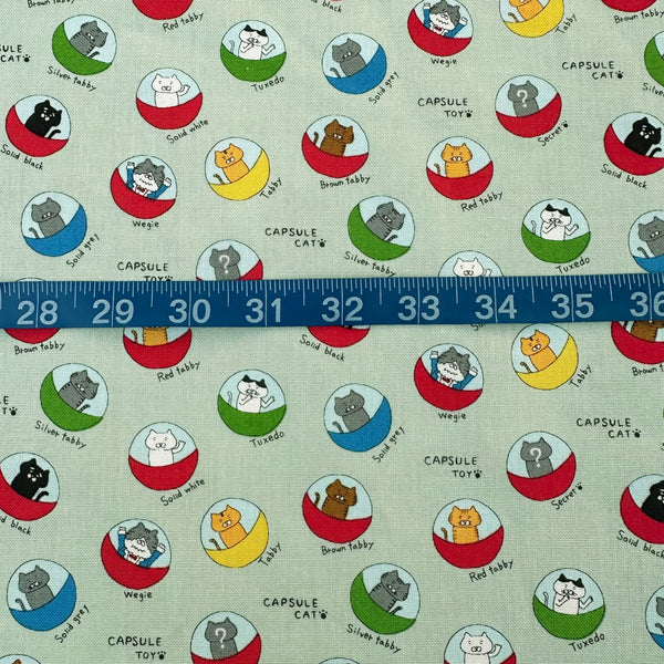 Scale of Capsule Toy Cats cotton canvas fabric in green by Cotton Kobayashi featuring playful cats inside capsule toy machines on a green background