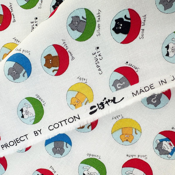 Selvage of Capsule Toy Cats cotton canvas fabric in white by Cotton Kobayashi featuring playful cats inside capsule toy machines on a white background