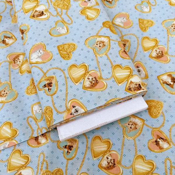Bolt of Cat Portrait Locket cotton fabric by Handworks featuring vintage-style cat portraits inside heart-shaped lockets on a blue background
