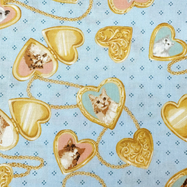 Close up of Cat Portrait Locket cotton fabric by Handworks featuring vintage-style cat portraits inside heart-shaped lockets on a blue background