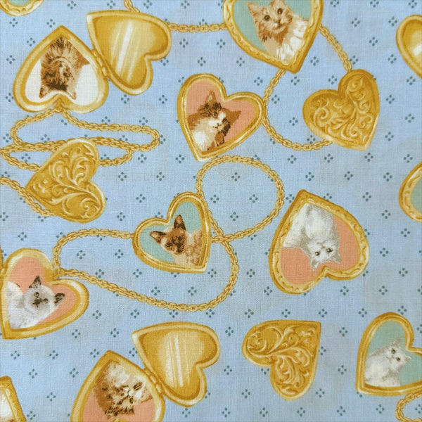 Cat Portrait Locket cotton fabric by Handworks featuring vintage-style cat portraits inside heart-shaped lockets on a blue background