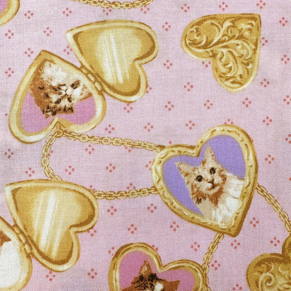 Close up of Cat Portrait Locket cotton fabric by Handworks featuring vintage-style cat portraits inside heart-shaped lockets on a pink background