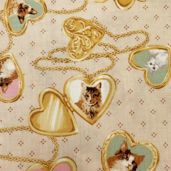 Close up of Cat Portrait Locket cotton fabric by Handworks featuring vintage-style cat portraits inside heart-shaped lockets on a tan background
