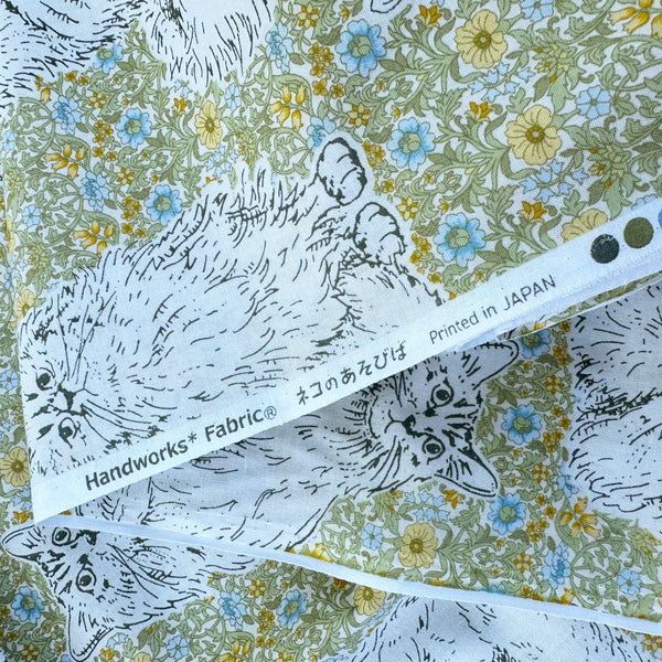 Selvage of Cats Playground cotton fabric in green and yellow by Handworks Japan featuring large-scale cats on a petite floral background