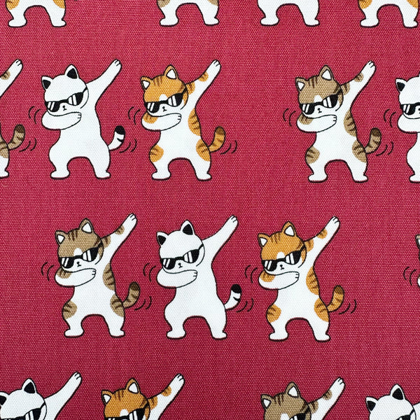 Close up of Dancing Cats wine cotton oxford fabric featuring a repeating pattern of cat motifs on a wine background.