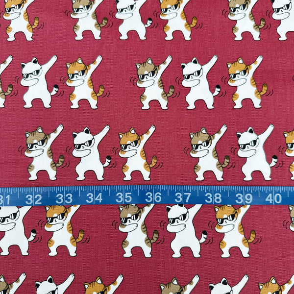 Scale of Dancing Cats wine cotton oxford fabric featuring a repeating pattern of cat motifs on a wine background.