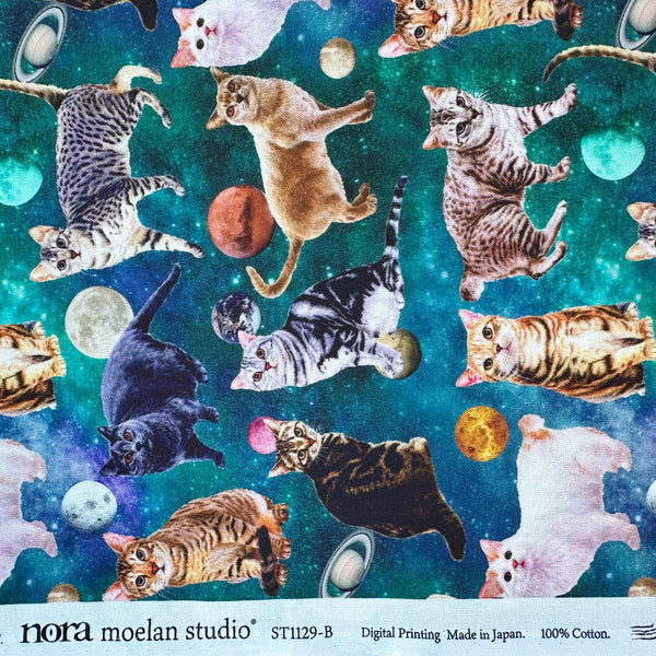 Selvage of Day Dream Cat cotton fabric in Teal by Nora featuring photo-real cats scattered among moons and planets on a teal sky background