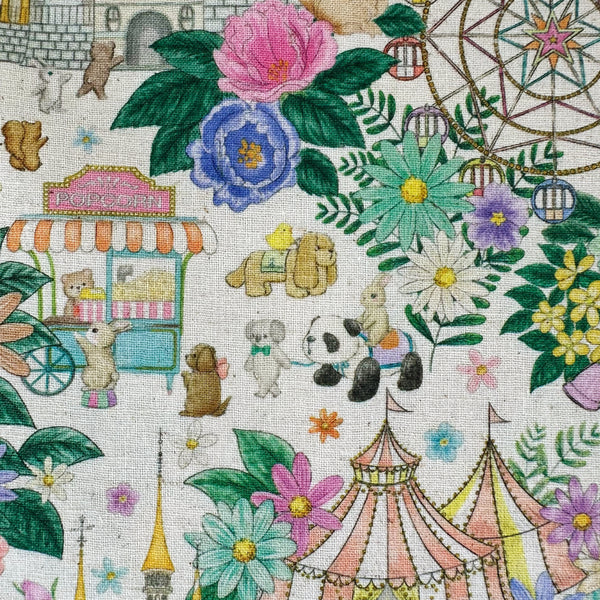 Close up of Decoration Park cotton linen fabric by Yukiemon for Hokkoh featuring a charming delicately illustrated vintage-style fun fair scene with florals, carousel rides, circus tents, and whimsical animals on a natural background, imported from Japan