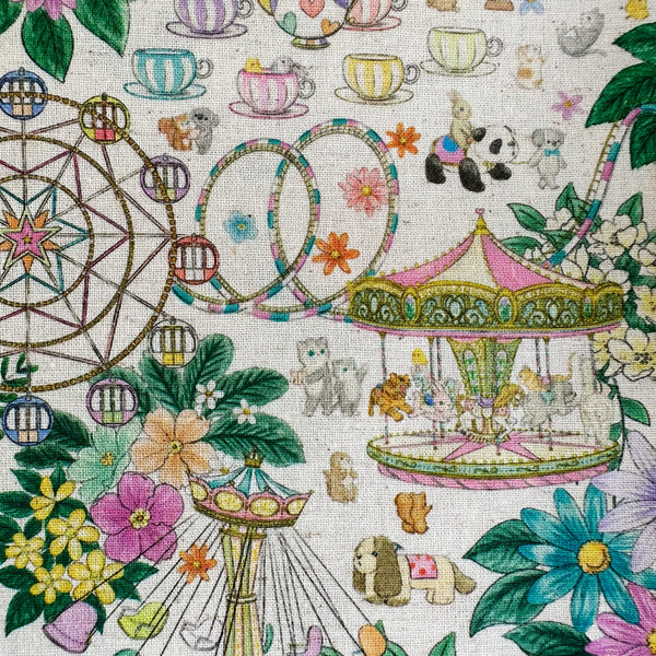 Close up of Decoration Park cotton linen fabric by Yukiemon for Hokkoh featuring a charming delicately illustrated vintage-style fun fair scene with florals, carousel rides, circus tents, and whimsical animals on a natural background, imported from Japan