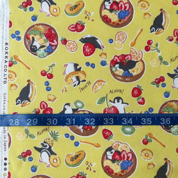 Delicious Animals Acai Bowl Penguin cotton oxford fabric by Kokka in yellow, style YGA-91070-2C, shown with a tape measure for scale