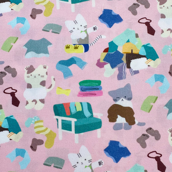 Dressed Up Cats cotton fabric in pink by Nora featuring playful cats trying on outfits, surrounded by laundry piles and scattered clothes
