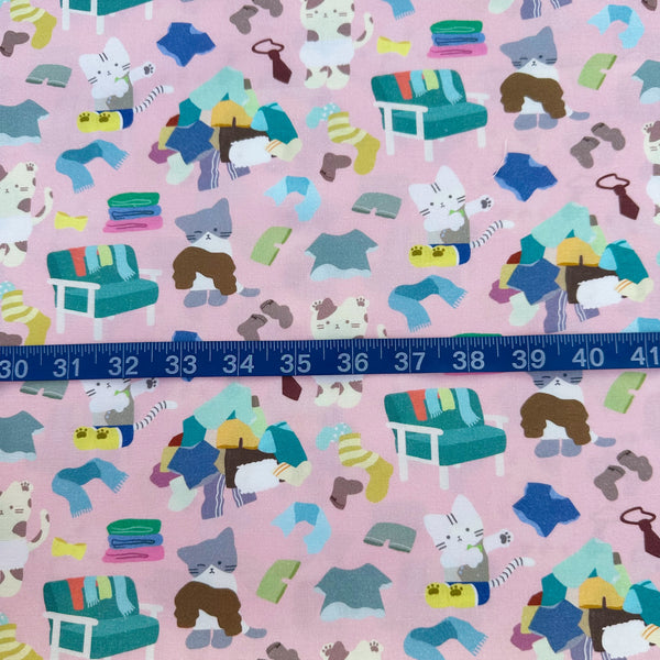 Scale of Dressed Up Cats cotton fabric in pink by Nora featuring playful cats trying on outfits, surrounded by laundry piles and scattered clothes
