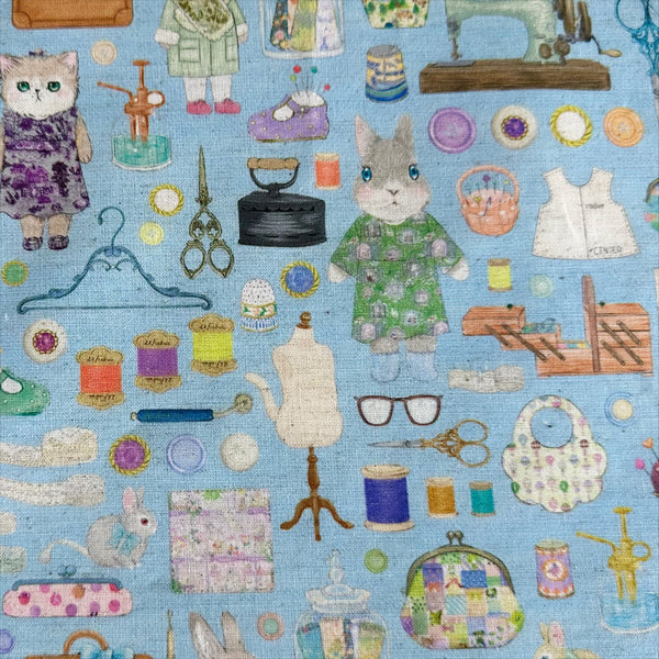 Dressmaker cotton linen fabric by Yukiemon for Hokkoh featuring delicately illustrated sewing notions, dressmaking tools, vintage sewing machines, and sweet bunny and kitty dressmakers on a blue background, imported from Japan