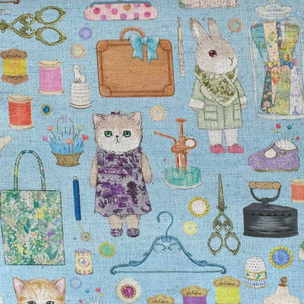 Close up of Dressmaker cotton linen fabric by Yukiemon for Hokkoh featuring delicately illustrated sewing notions, dressmaking tools, vintage sewing machines, and sweet bunny and kitty dressmakers on a blue background, imported from Japan