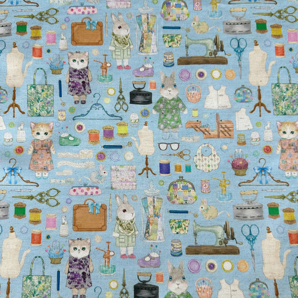 Dressmaker cotton linen fabric by Yukiemon for Hokkoh featuring delicately illustrated sewing notions, dressmaking tools, vintage sewing machines, and sweet bunny and kitty dressmakers on a blue background, imported from Japan