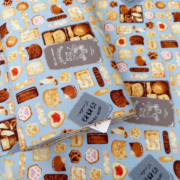 Bolt of Neko Cookie Can cotton Oxford fabric by Komu Strada featuring cat-shaped cookies, biscuits, and cookie tins on a blue background