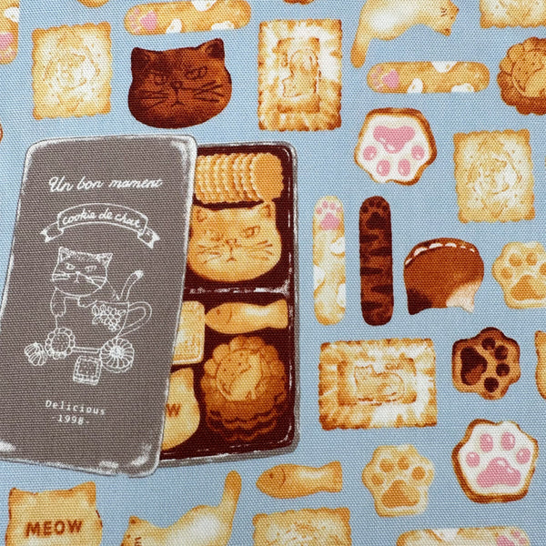 Close up of Neko Cookie Can cotton Oxford fabric by Komu Strada featuring cat-shaped cookies, biscuits, and cookie tins on a blue background