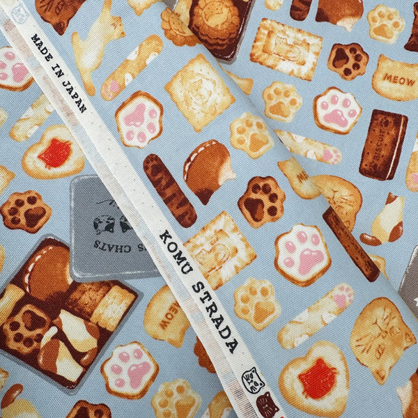 Selvage of Neko Cookie Can cotton Oxford fabric by Komu Strada featuring cat-shaped cookies, biscuits, and cookie tins on a blue background