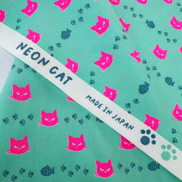 Selvage of Neon Cat Cotton Oxford Fabric in Aqua featuring a playful print of fish, paws, and neon cat faces, imported from Japan.