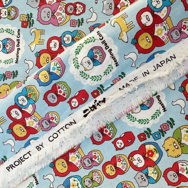 Selvage of Nesting Dolls Cats Cotton Canvas Fabric by Cotton Kobayashi, style KTS-7177C, featuring cat nesting doll illustrations, in blue, imported from Japan