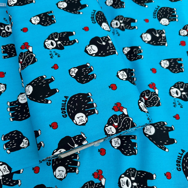 Bolt of Silly Gorilla Cotton Oxford Fabric in Blue by Cosmo Textiles featuring animated gorillas and apples on a blue background.