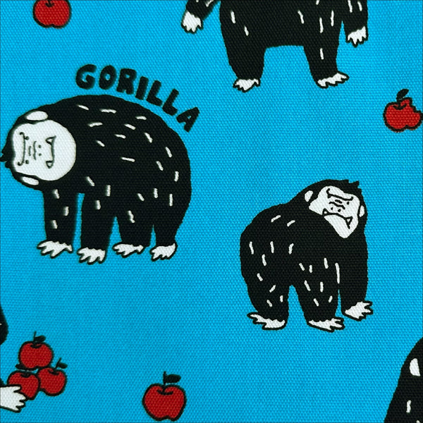 Close up of Silly Gorilla Cotton Oxford Fabric in Blue by Cosmo Textiles featuring animated gorillas and apples on a blue background.