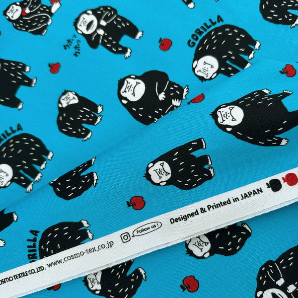 Selvage of Silly Gorilla Cotton Oxford Fabric in Blue by Cosmo Textiles featuring animated gorillas and apples on a blue background.