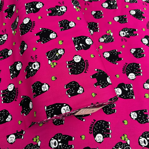 Bolt of Silly Gorilla Cotton Oxford Fabric in Pink by Cosmo Textiles featuring animated gorillas and apples on a pink background.
