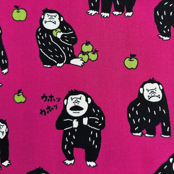 Close up of Silly Gorilla Cotton Oxford Fabric in Pink by Cosmo Textiles featuring animated gorillas and apples on a pink background.