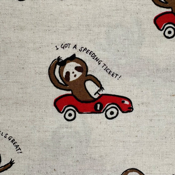 Close up of Speedy Sloth Cotton Linen Blend Fabric by Cosmo Textiles, style AP65204 2A, featuring sloths in red racing cars, in natural