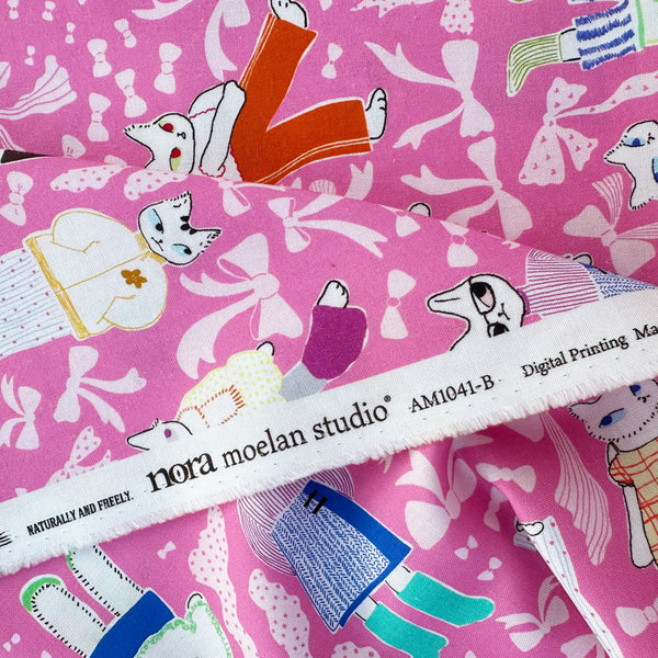 Selvage of The Open Closet cotton fabric in pink by Nora featuring cats getting dressed in cute outfits with bows imported from Japan